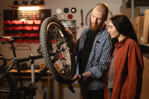 Two person examine bicycle wheel in repair workshop. Woman Assisting her husband Professional Repairman in Bike Fixing. Bike Maintenance and repair Concept