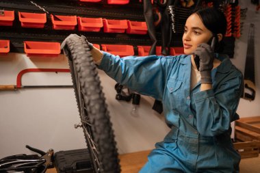 Kadın tamirci müşteriyle telefonda konuşuyor, hasarlı bisikleti tamir ediyor. Boşluğu kopyala