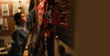 Bir bisiklet tamircisinde kadın tamircinin duvardaki aletlere ve ekipmanlara bakışını. Pankart. Boşluğu kopyala