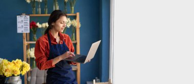 İspanyol iş kadını çiçek dükkanı sahibinin portresi elinde dizüstü bilgisayarla elinde çiçeklerle ekrana bakıyor. Kadın çiçekçi bilgisayar kullanarak çalışıyor. Pankart. Boşluğu kopyala