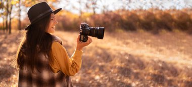 Genç bayan fotoğrafçı sonbahar ormanında doğanın fotoğrafını çekiyor. Pankart. Boşluğu kopyala