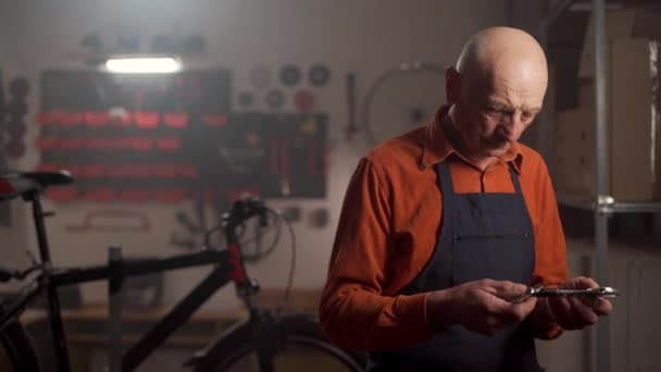 Yaşlı Tamirci Elinde Ayarlanabilir Anahtarlarla Kameraya Bakarak Bisikleti Tamir Ediyor — Stok video