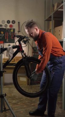 Beyaz erkek işçi bisikleti tamir ediyor. Motosiklet atölyesi ya da garaj içi. Dikey video