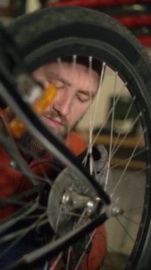 Depoda bisiklet tamir eden sakallı bir tamirci vitesi yağlar ve tekerlekteki zinciri yağlar. Yakın plan. Dikey video
