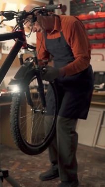 Yaşlı adam bisiklet tamircisi atölyede çalışıyor, tekerlekleri tamir ediyor. Uzayı kopyala Dikey görünüm