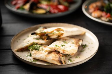 Erimiş süluguni peynirli lavaş ekmeği otlarla süslenmiş beyaz bir tabakta servis edilir. Boşluğu kopyala