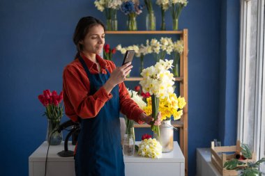 Mutlu, gülümseyen İspanyol kadın çiçek buketi siparişi için fotoğraf çekiyor. Çiçekçide çalışan serbest çalışan bir çiçekçi. Boşluğu kopyala
