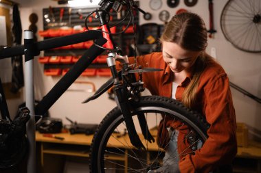 Atölyedeki bisiklet iskeletinin yanındaki beyaz kadın tamircinin portresi. Kadın üstat, bisiklet tamir uzmanı, atmosferik garajda bisiklet tamircisi. Boşluğu kopyala