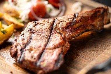 Ahşap tahtada, patatesli ve domatesli kuzu pirzolası, yakın plan.