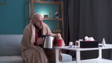 Hasta adam evdeki kanepede oturup sıcak çay hazırlıyor ve içiyor. Sağlık, hastalık ve insan kavramı.