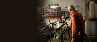 Garajda veya atölyede bisiklet tamir eden yaşlı bir tamirci. Bisiklet bakım ve montaj konsepti. Pankart. Boşluğu kopyala