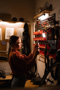 Atölyede bisiklet tamir eden kadın tamirci, garajda aletlerle duvarın yanında duran kadın. Bisiklet bakım konsepti. Boşluğu kopyala