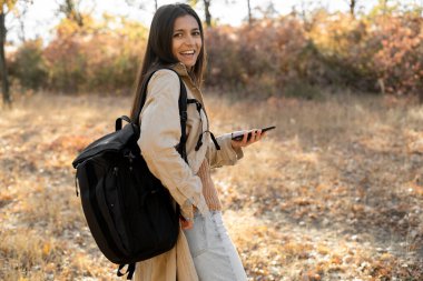 İspanyol kadının SMS yazarken fotoğrafı çanta taşırken, sonbahar kıyafetleri giyerken açık havada parkta yürürken. Boşluğu kopyala