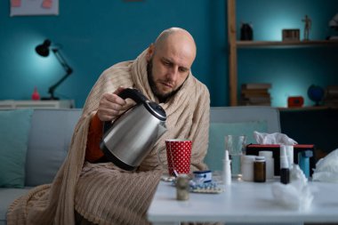 Soğuk ve yüksek ateşten muzdarip bir adam fincana çay döker. Evde grip tedavisi konsepti. Boşluğu kopyala