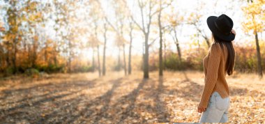 Ağaçların önündeki sonbahar parkında dikiz manzaralı güzel bir kadın. Boşluğu kopyala