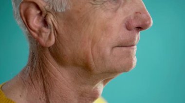 Yaşlı bir adam mavi arka planda izole edilmiş bir şişeden su içer. Sağlık ve hidrasyon konsepti. Boşluğu kopyala