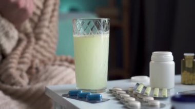 Akşamdan kalma ya da baş ağrısı çeken bir adam ağrı kesici tabletle su içiyor. Yakın plan.