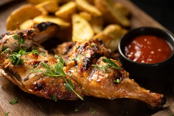 Baked chicken leg with fries potatoes on wooden board. Baking dish on table, close-up. Grilled chicken legs.