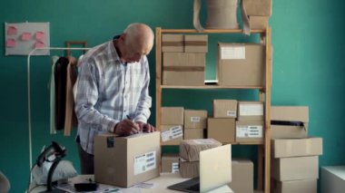 Başlangıçta küçük işletme KOBİ 'si, çevrimiçi giyim mağazası sahibi yaşlı bir adam alışveriş siparişini kontrol ediyor ve paket ürün kutusu hazırlıyor. Boşluğu kopyala