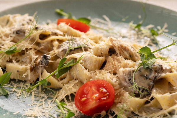 Traditional Italian fettuccine pasta with mushrooms and fried chicken in a creamy sauce with tomatoes on a plate. Close-up