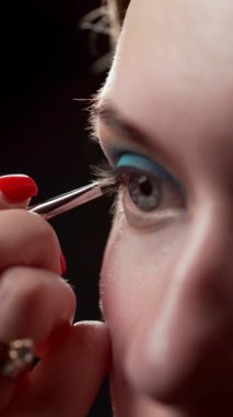 Profesyonel bir makyaj sanatçısı, modelin gözlerinin ifade ediciliğini vurgulamak için üst göz kapağının mukoza zarını çizmek için koyu gölgeli bir fırça kullanır. Aydınlık akşamın süreci