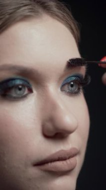 Bir makyöz, kalıcı makyajdan sonra temiz ciltli güzel bir beyaz modelin kaşlarını tarar. Makyaj ve kozmetoloji kavramı, kaşların şeklini modelleme..