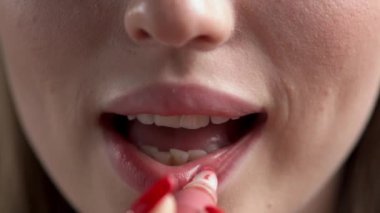 Bir kadının eli, dudaklarının üst ve alt kısımlarına doğal renkte ruj sürüp dudaklarını seksi bir şekilde şaplaklıyor..
