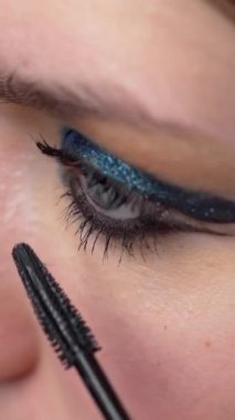 Güzellik salonunda makyaj yapıyorum. Makyaj fırçasıyla alt kirpiğe siyah rimel süren profesyonel bir makyözün yakın çekimi. Kadın gözü. Kirpikleri kapladıktan sonra uzatmak.