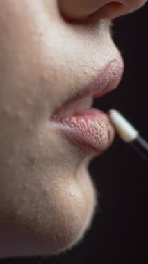 Bir kadının elinin yandan görünüşü, dudakları açık, üst ve alt dudaklarına fırça sürerek doğal renk ruj sürüyordu. Moda perde arkasında. Güzellik salonu..