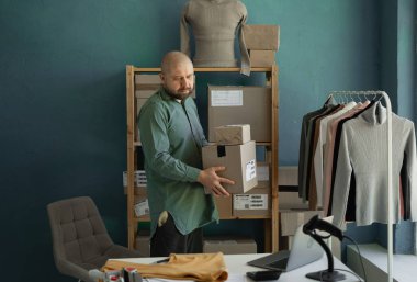 Satıcı elinde karton kutular tutuyor ve not defteriyle paket göndermek için adresleri kontrol ediyor. Elbise teslimatı. Küçük bir iş. Boşluğu kopyala