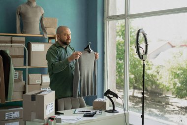 Blogcu elinde süveter tutuyor ve müşterilerine yeni kıyafetlerin geldiğini söylüyor. Mal teslimatı. Boşluğu kopyala