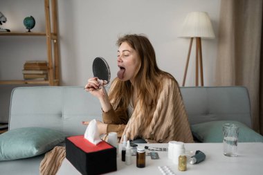 Boğaz ağrısı. Kız elinde bir ayna tutuyor ve boğazına bakıyor. Acı çekiyor ve yutkunuyor. Evde, kanepede, battaniyeye sarılmış bir şekilde oturuyor. Soğuk kavram.