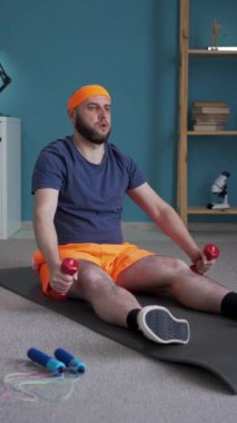 Kilolu adam evde spor egzersizleri yapıyor. Bir kişi dambıl kullanarak spor yapıyor. Zindelik ve kilo kaybı kavramı