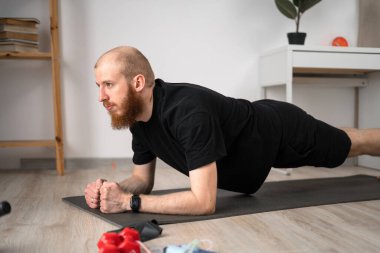 Bir adam, gücünü ve dayanıklılığını arttırmak için evde kalas egzersizleri yapar.