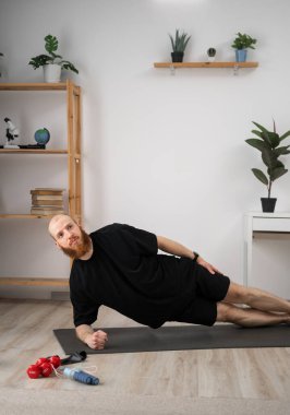 Sakallı genç adam evde spor yapıyor yan yatmış kameraya bakıyor. ev sporu konsepti. Boşluğu kopyala