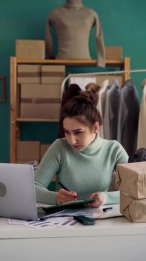 Lojistik, dizüstü bilgisayar ve perakende veya butik mağazasının moda müdürü listedeki kutulardaki giyim stoklarını kontrol ediyor. Küçük işletmeler, girişimciler ve mağazada elbise envanteriyle çalışan genç kadınlar.