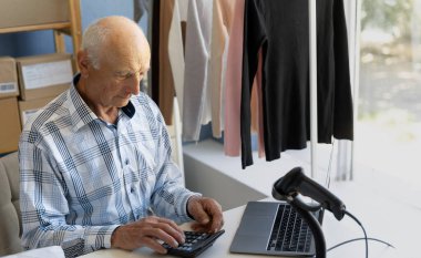 Küçük işletme sahibi, girişimci, ciddi bir işadamı faturaları kontrol ediyor, kârı hesaplıyor, faturaları ödüyor, kendi şirketinin finans işlerini yönetiyor, dizüstü bilgisayarla masada oturuyor, depoda belgeleri tamamlıyor. Boşluğu kopyala