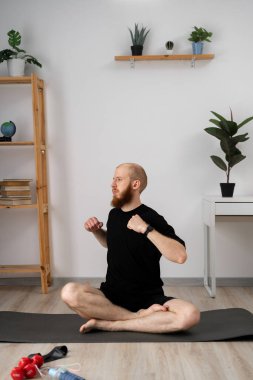 Bir adam minimalist dekorlar ve rahatlatıcı bir atmosferde bitkilerle çevrili evde yoga yapıyor.