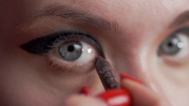Bir kadın titizlikle siyah göz kalemi sürüyor, göz makyajı için profesyonel tekniğini sergiliyor. Yakın plan.