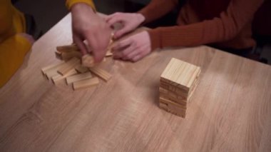 İki kişinin elleri masa başı tahta blok oyununda, bir kule inşa etmeye odaklanmış, kapalı alanda gevşemeye. Boşluğu kopyala