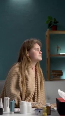 Sıcak bir battaniyeye sarılmış genç bir kadın, evinde kendini kötü hissediyor, çevresindeki rahatlığı ve rahatlığı arıyor.