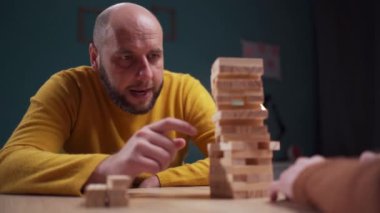 Sarı kazaklı bir adam evde tahta blok oyunu oynuyor, strateji kuruyor ve istifliyor. Boşluğu kopyala