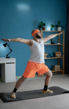 Parlak spor kıyafetleriyle evde yoga yapan bir adam modern ortamlarda denge ve zindelik sergiliyor..