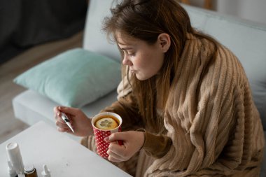 Hasta kadın ateşini ölçüyor ve soğuk için limonlu çay içiyor. Virüs enfeksiyonu. Boşluğu kopyala