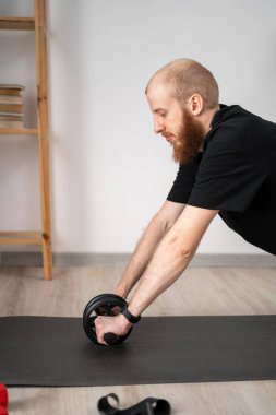 Kaslı adam kol kaslarını tekerlekle çalıştırıyor. Evde fitness var. Aktif yaşam tarzı. Boşluğu kopyala