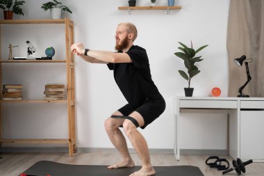 Siyah spor giyimli atletik adam antrenman yapıyor, evde mekik çekiyor, konsantre görünüyor. Boşluğu kopyala