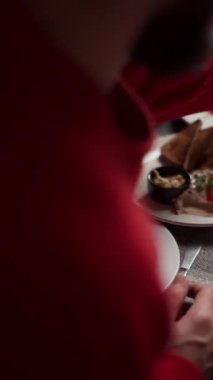 Kırmızı tişörtlü bir adam bir restoranda tabak ve sofra takımı olan bir masada yemek yiyor. Yakın çekim.