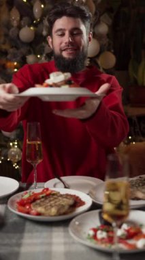 Kırmızı kazaklı bir adam arkadaşlarıyla ve lezzetli yemeklerle çevrili şenlikli bir akşam yemeğinin tadını çıkarıyor. Dikey video