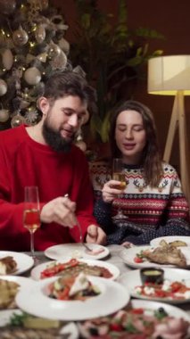 Sıcak bir evin sıcaklığında arkadaşlarla Noel yemeğinin tadını çıkaran bir çift. Dikey video