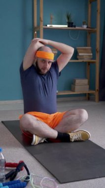 Çekici sporcu adam evde yoga minderinin üzerinde ısınma egzersizleri yapıyor. Erkek sporcu antrenman yapıyor. Dikey video